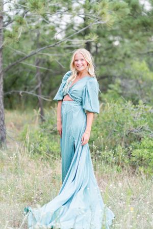 An elegant pose in a flowing light blue dress set against wild grasses and pine trees.