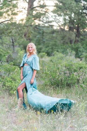 A whimsical pose in a flowing turquoise dress with boots in a natural forest setting.
