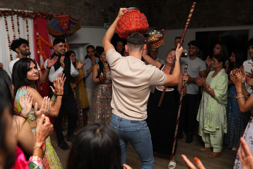 Wedding guests dance and celebrate while someone holds up decorative props during an indoor celebration.