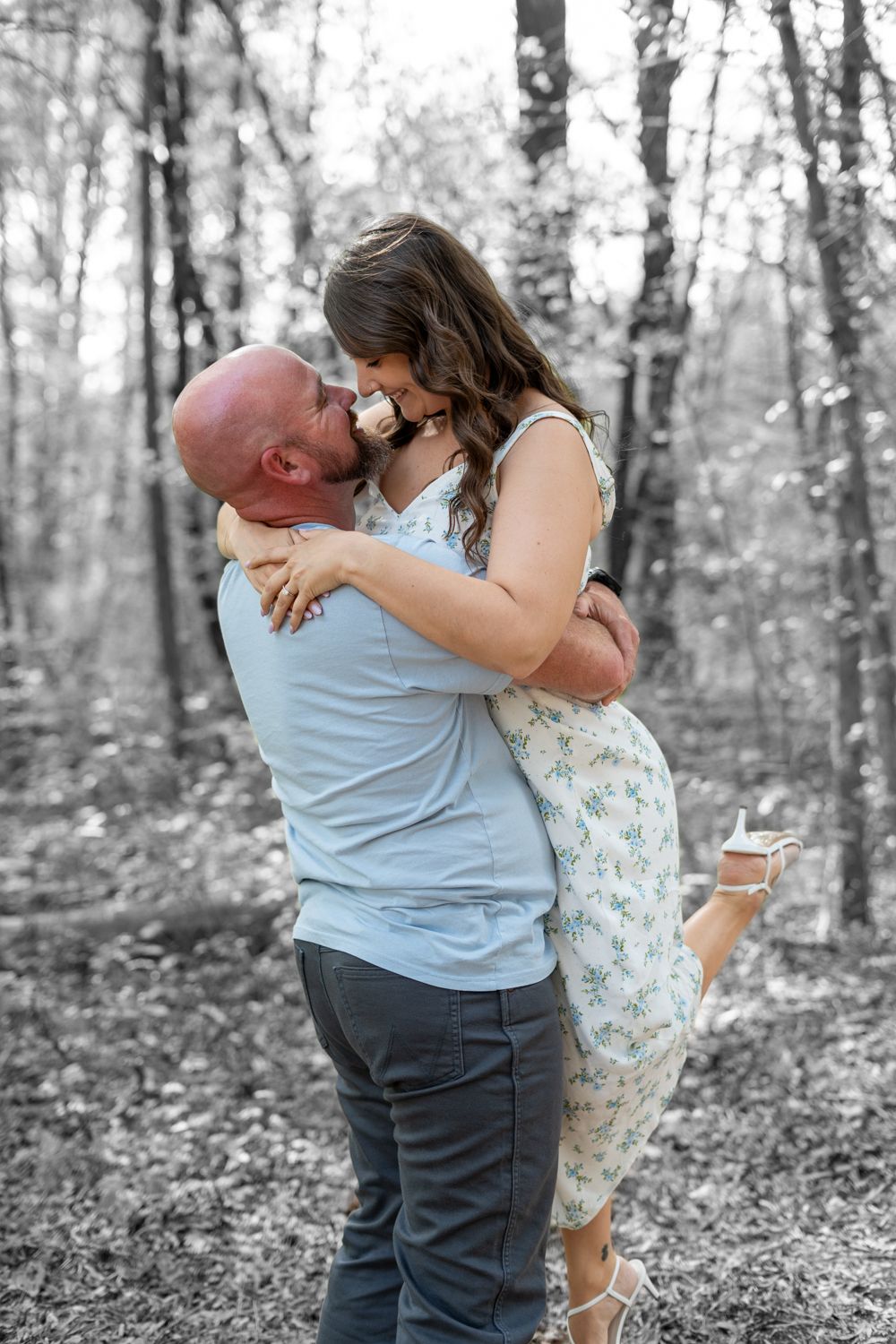 A joyful candid moment from an outdoor engagement session featuring a man lifting his fiancée in his arms.