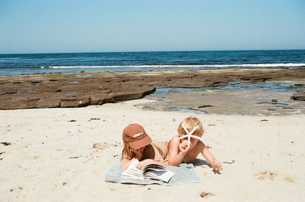 People relax and sunbathe on a sandy beach with blue ocean waves in the background on a sunny summer day.