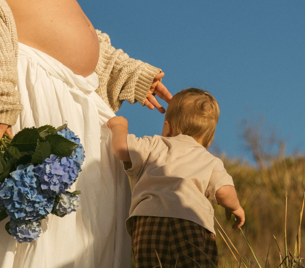 A person in a white dress holds a bouquet of blue hydrangeas while walking through a golden field at sunset.
