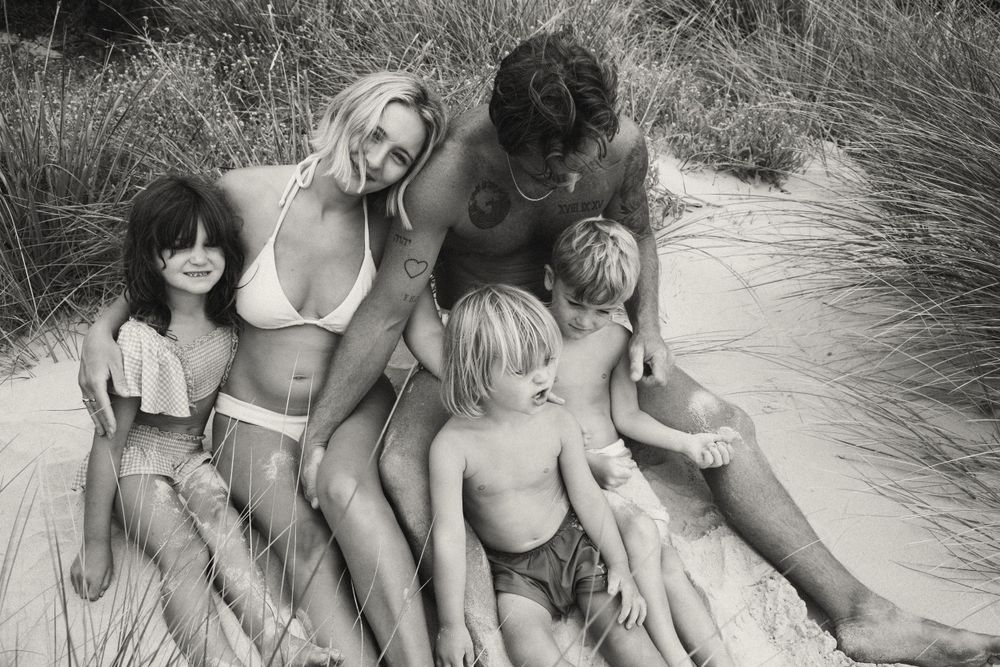 Family relaxing together on sandy beach dunes in black and white photograph.