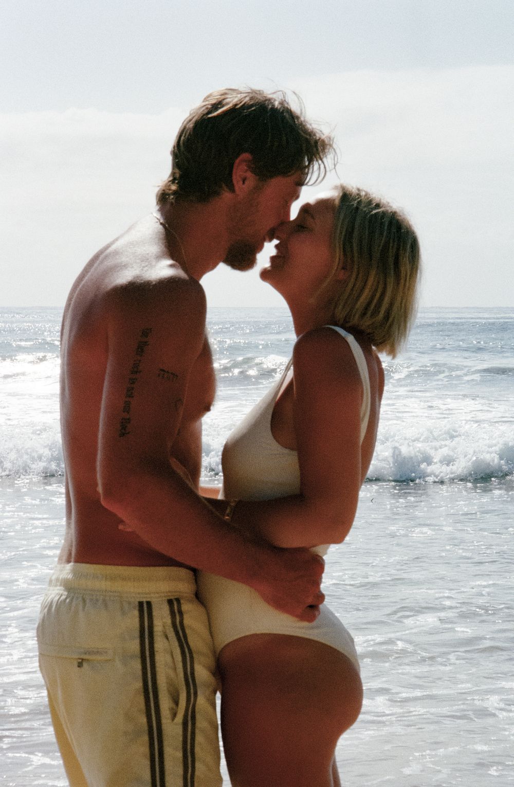 A couple shares an intimate moment while standing in the ocean waves at the beach.
