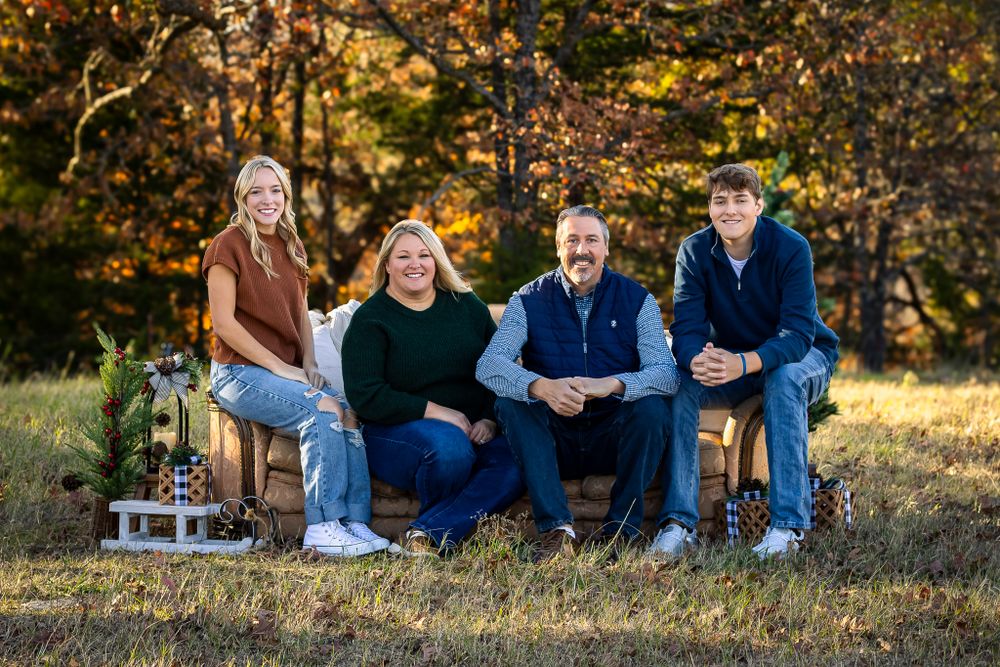 Family of four sits together on wooden chairs for outdoor portrait session in autumn setting.