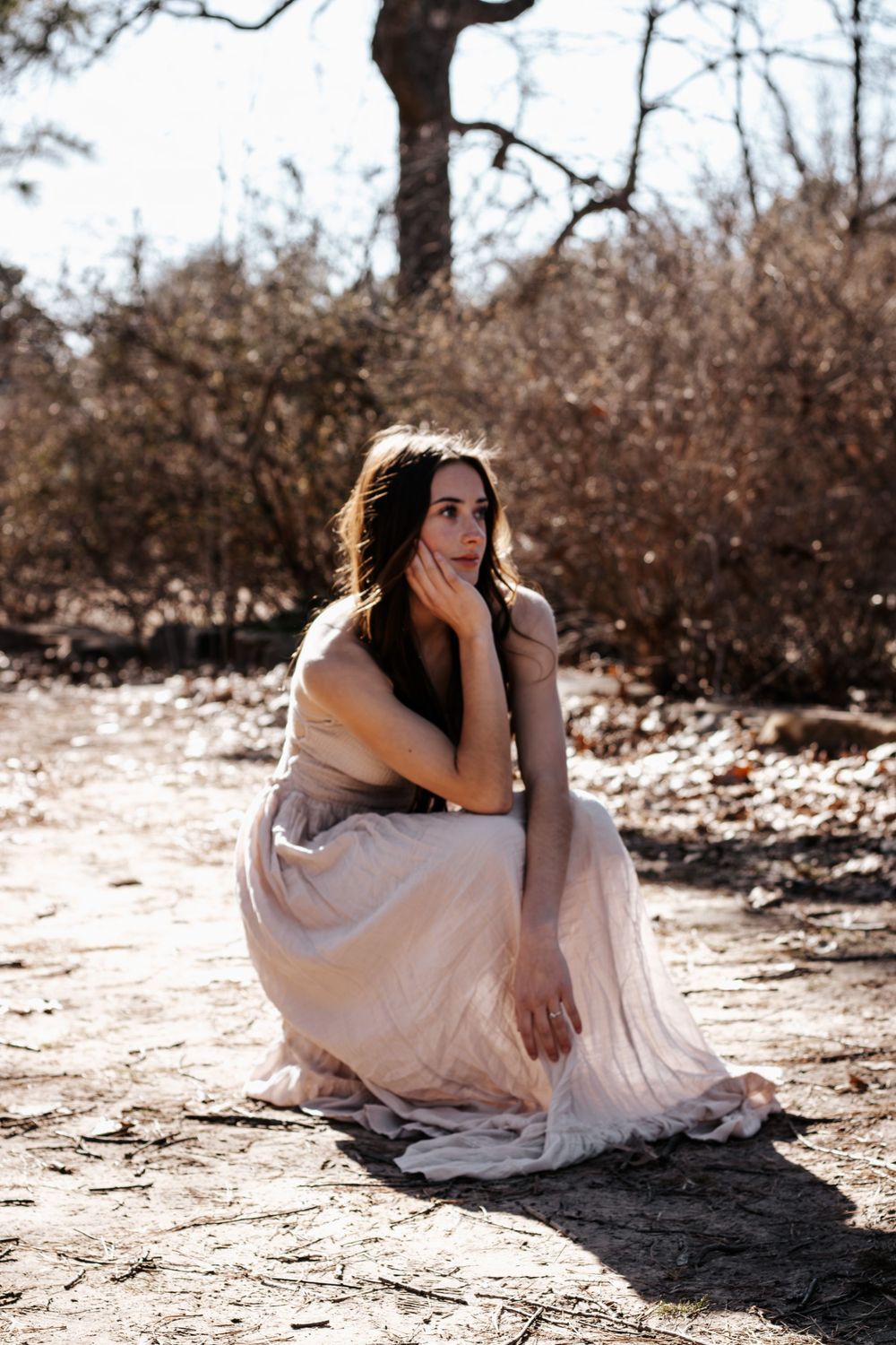 Portrait session featuring person in flowing dress seated on natural terrain during golden hour.