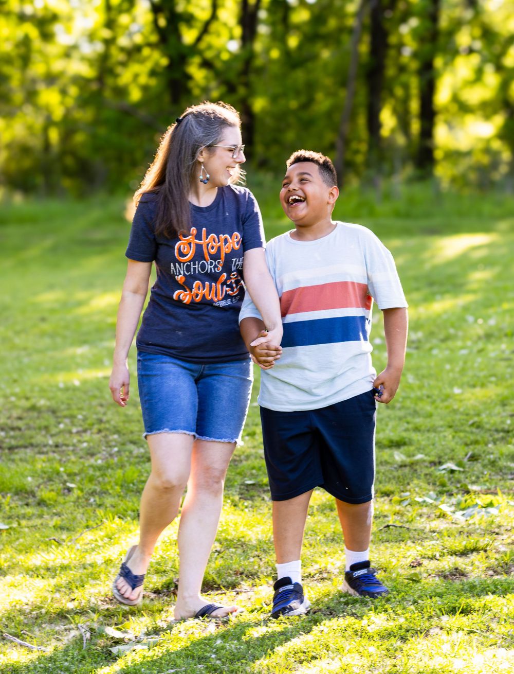 A pair walking together and sharing a joyful laugh while strolling on green grass in a sunlit park setting.