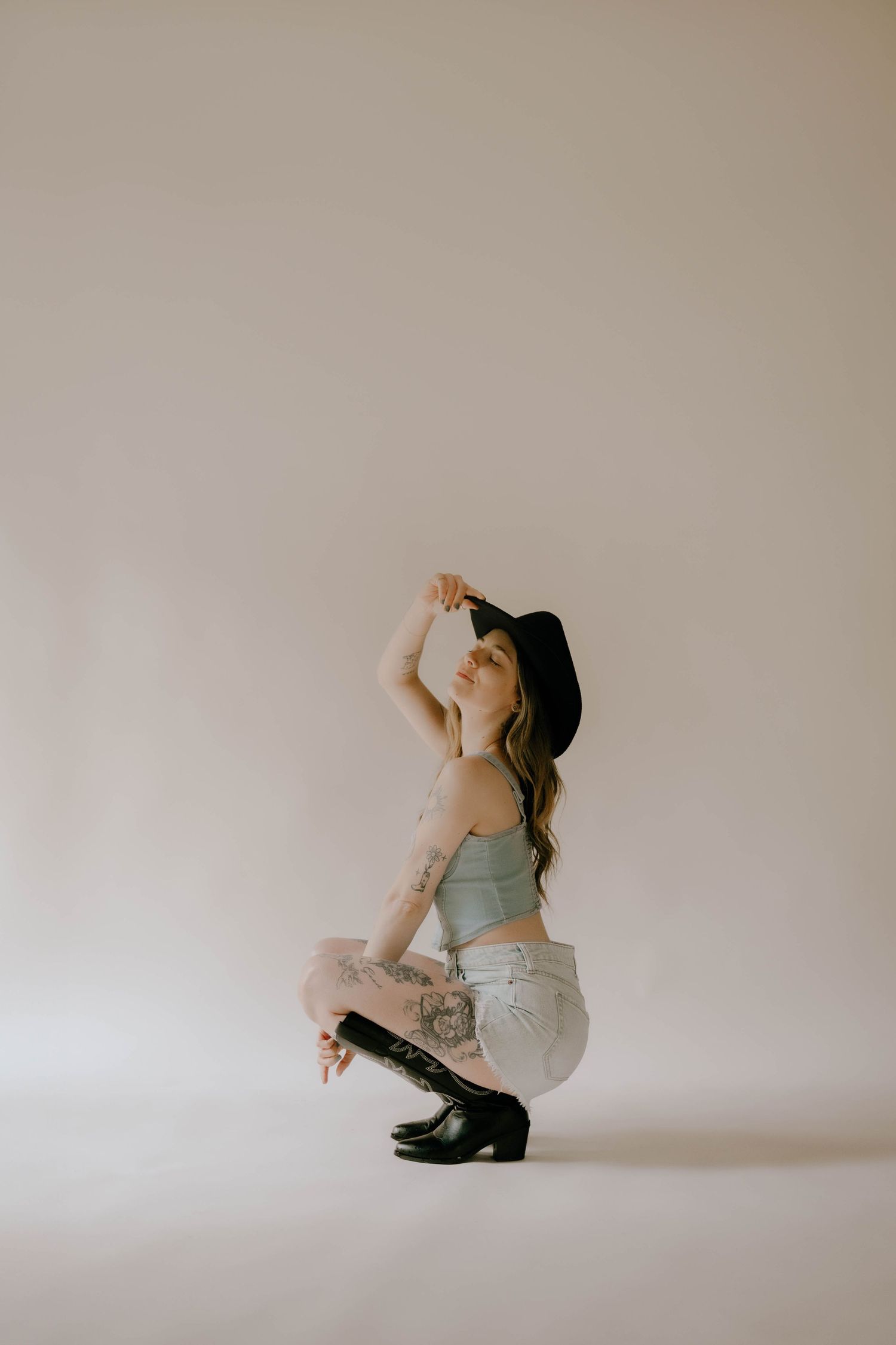 Artistic portrait of someone in casual wear and black hat crouching against white backdrop.