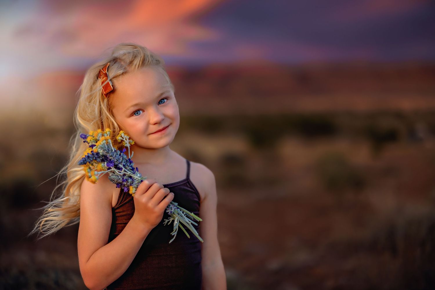 Young girl holding wildflowers against desert sunset backdrop.