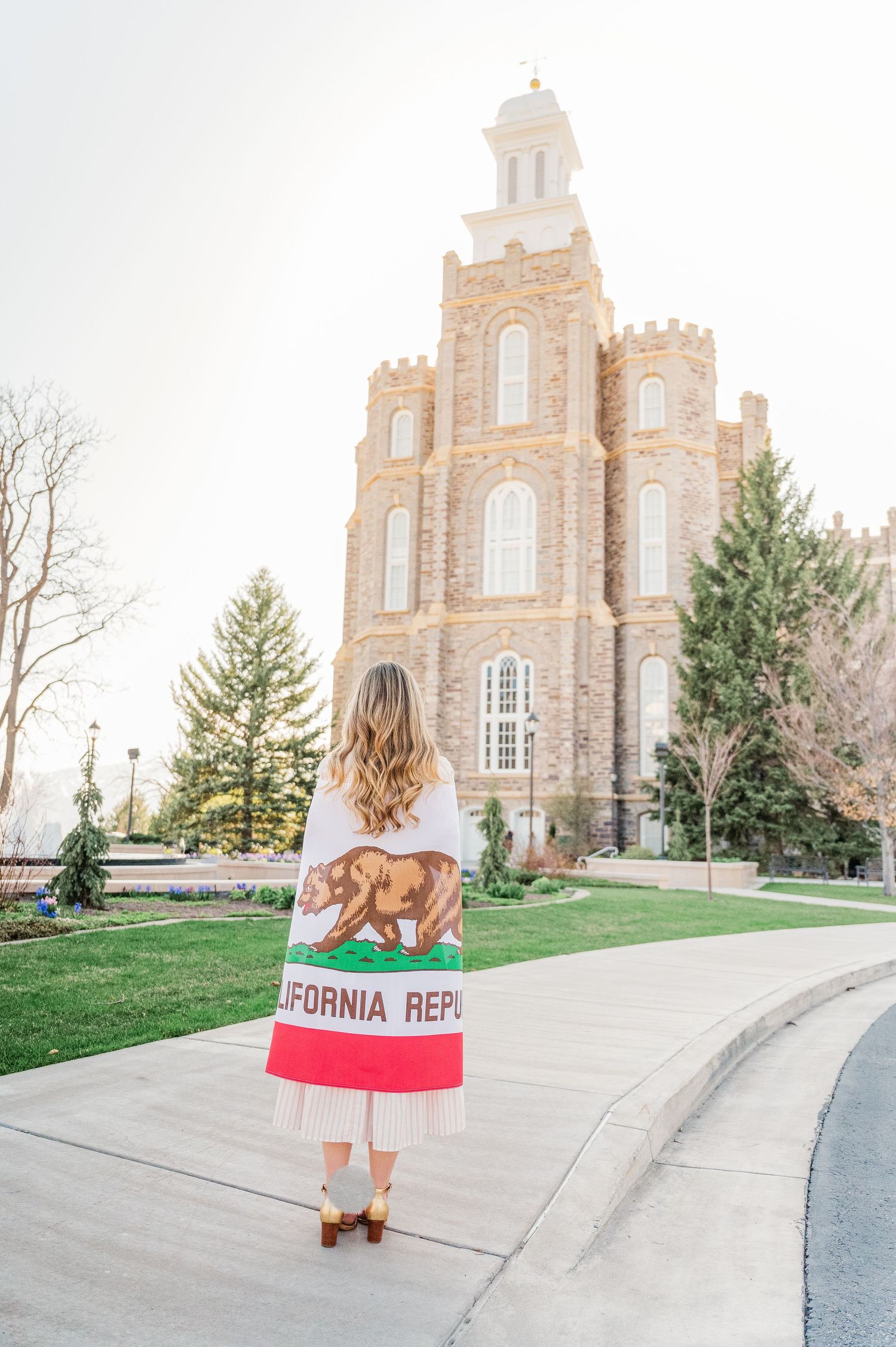 Person holding California flag stands in front of stone temple building with tower.