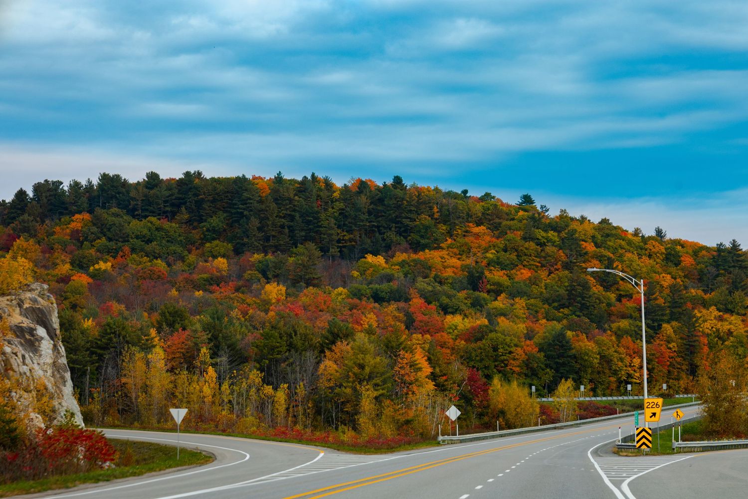 Scenic autumn road winding through colorful fall foliage under a bright blue sky.