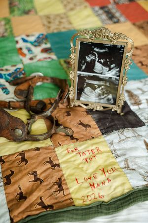 Ultrasound photo in ornate gold frame on patchwork quilt with handwritten note reading For Tater Tot Love You Nana 2026.