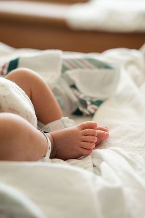 Close-up of tiny newborn baby feet resting on white hospital blankets in soft warm light.