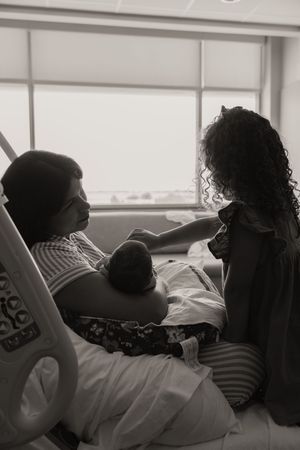 Black and white photo of mother in hospital bed holding newborn while young girl looks on.