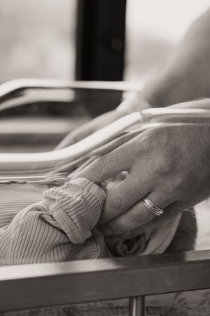 Black and white photo of a parent's hand with wedding ring gently holding a newborn baby's tiny hand during Fresh 48 session.