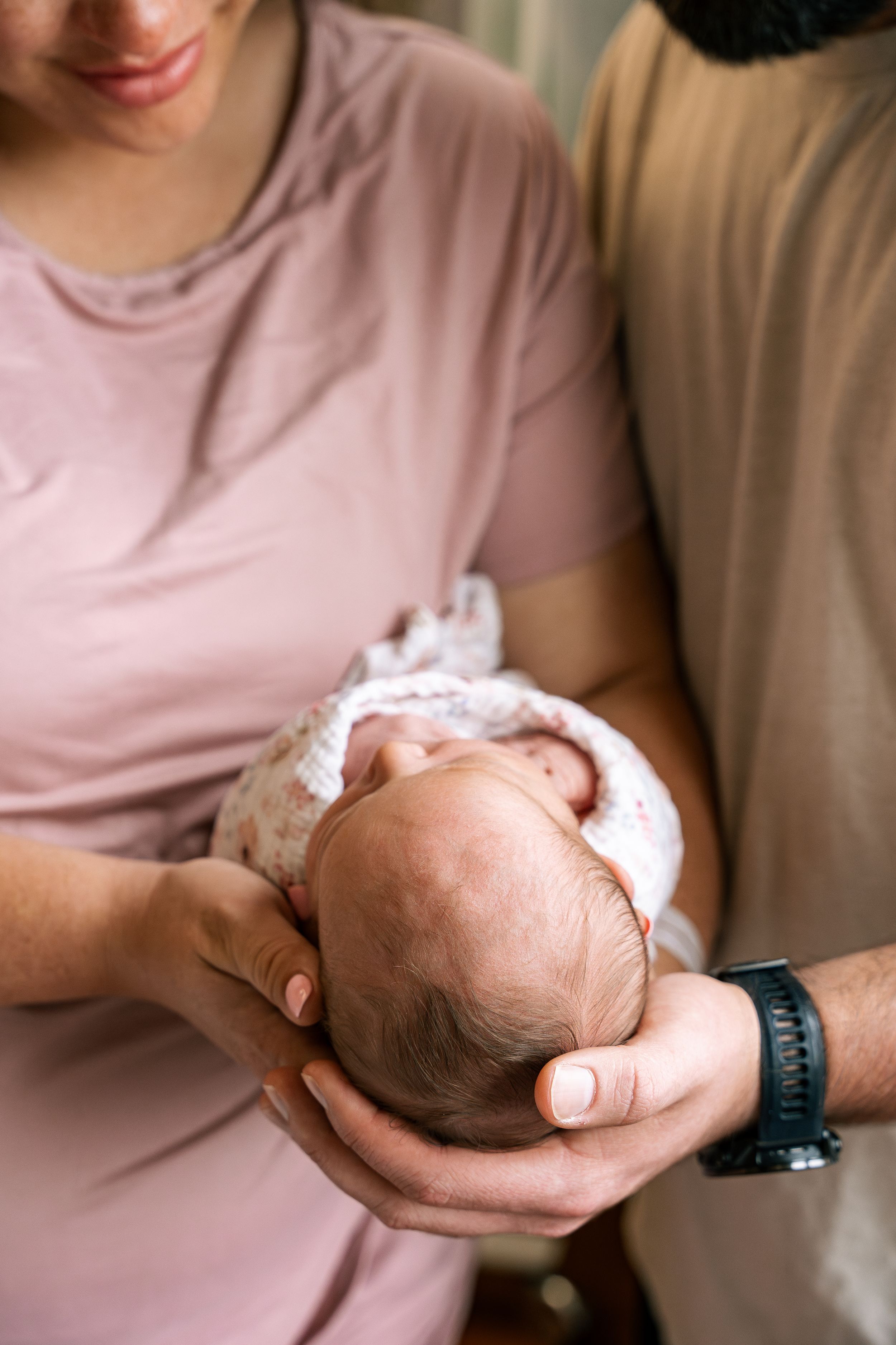 Two parents carefully cradling a sleeping newborn baby together in their hands in Fresh 48 session in hospital.