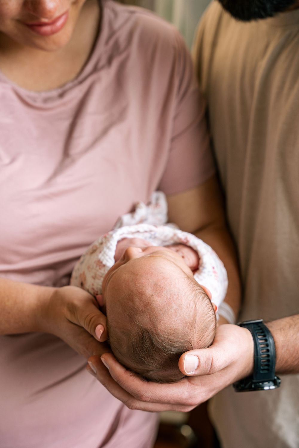 Two parents carefully cradling a sleeping newborn baby together in their hands in Fresh 48 session in hospital.