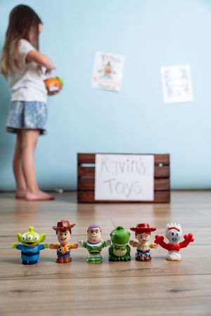 Toy Story Little People figures lined up on floor with child and Kevin's Toys box behind during 1st birthday session.
