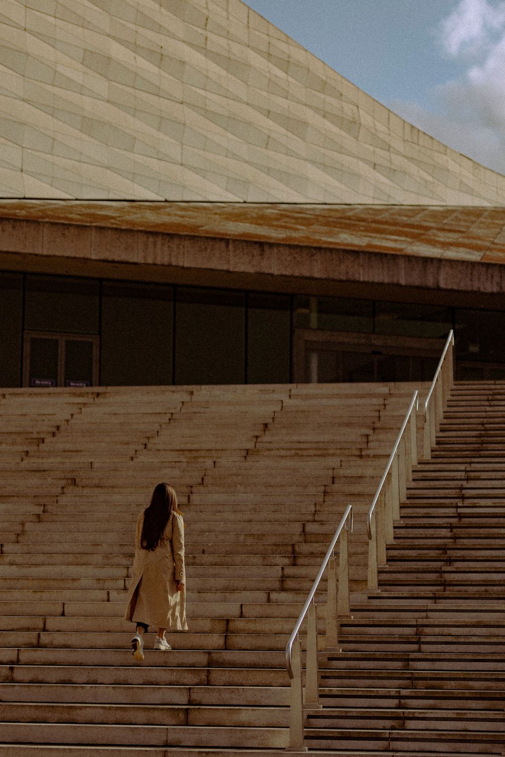 Person in light coat descending concrete stadium steps in sepia tones.