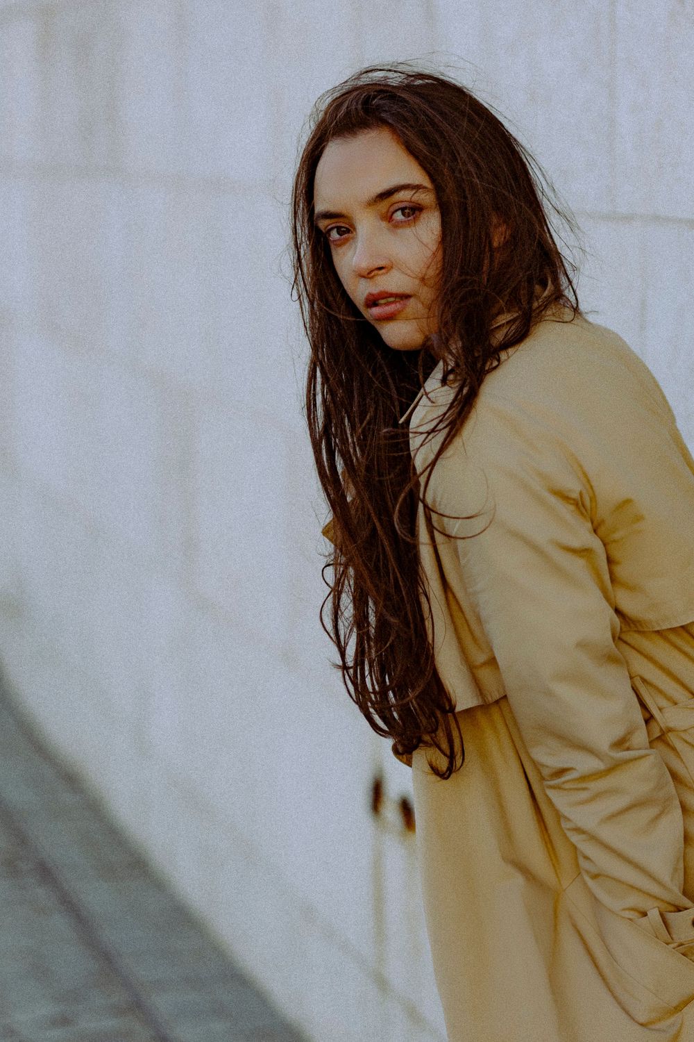 Dramatic fashion pose against white wall showcasing beige outerwear.