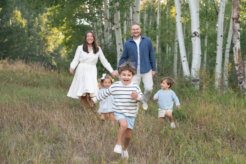 A family in white and blue outfits walks through a sunlit aspen forest during a photo session in Vail Colorado