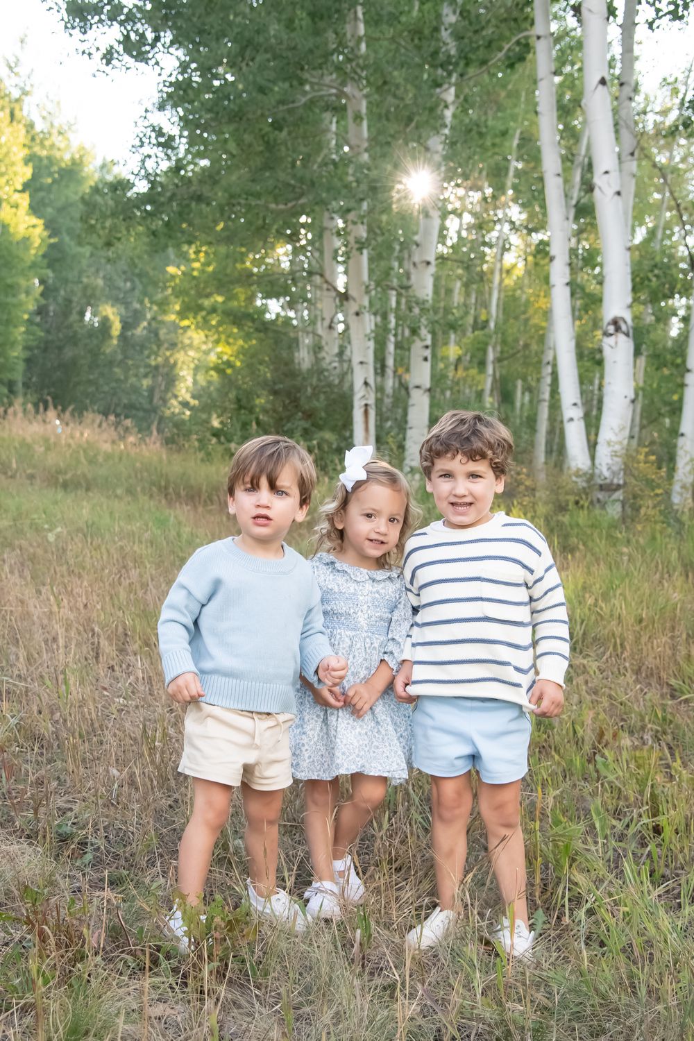 Children sit together in a scenic aspen grove wearing coordinated white and striped outfits during an outdoor photoshoot in Vail Colorado