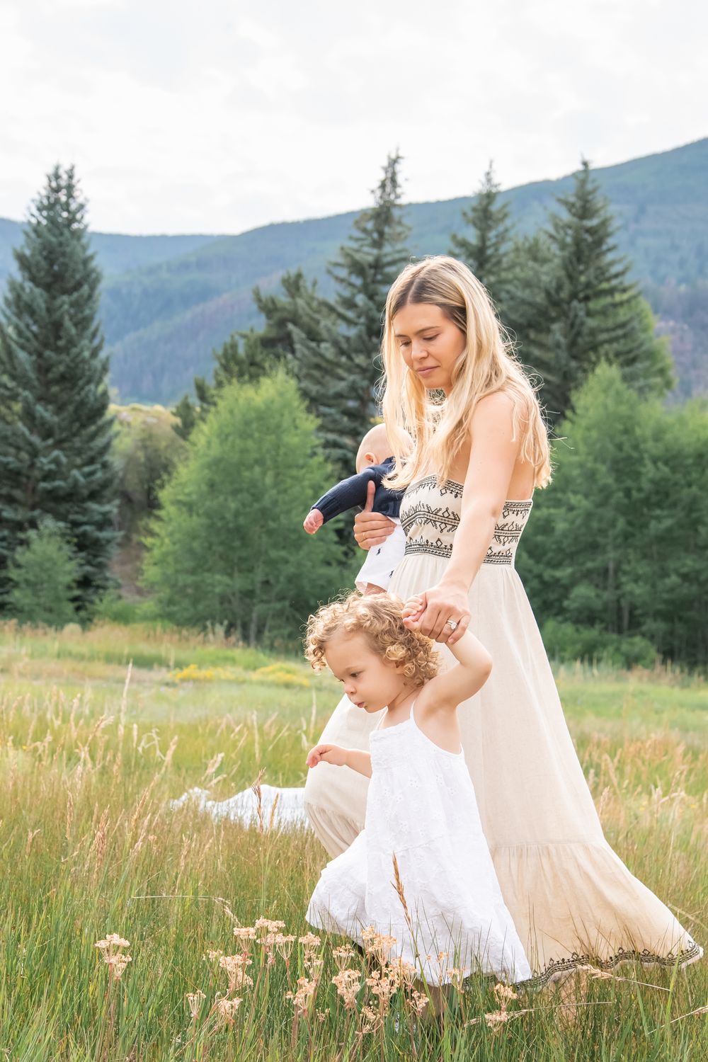 Sweet and whimsical photo session with mother walking through grass with her daughter in white flowy dresses.