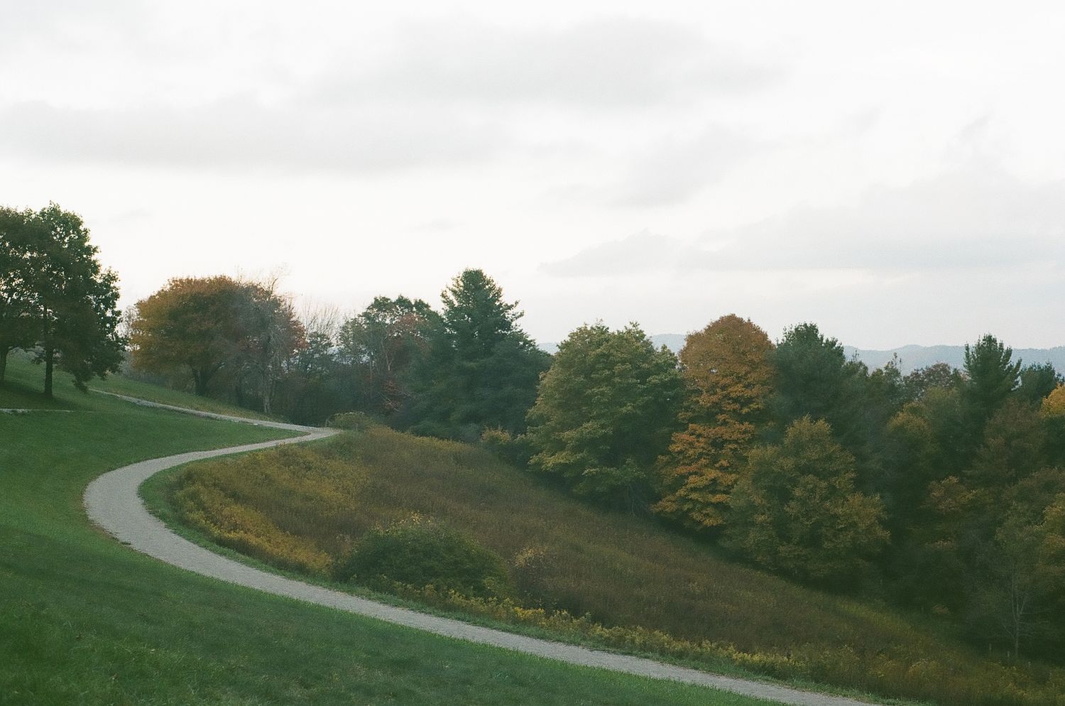 A winding gravel path curves through green hillsides with colorful fall foliage in the background.