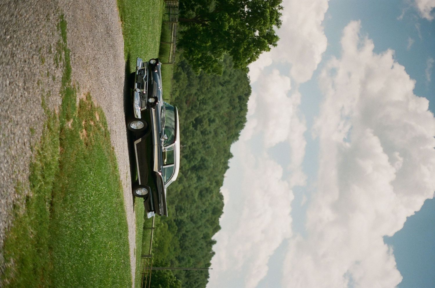 A classic vintage car parked on grass against a backdrop of blue sky and white puffy clouds.