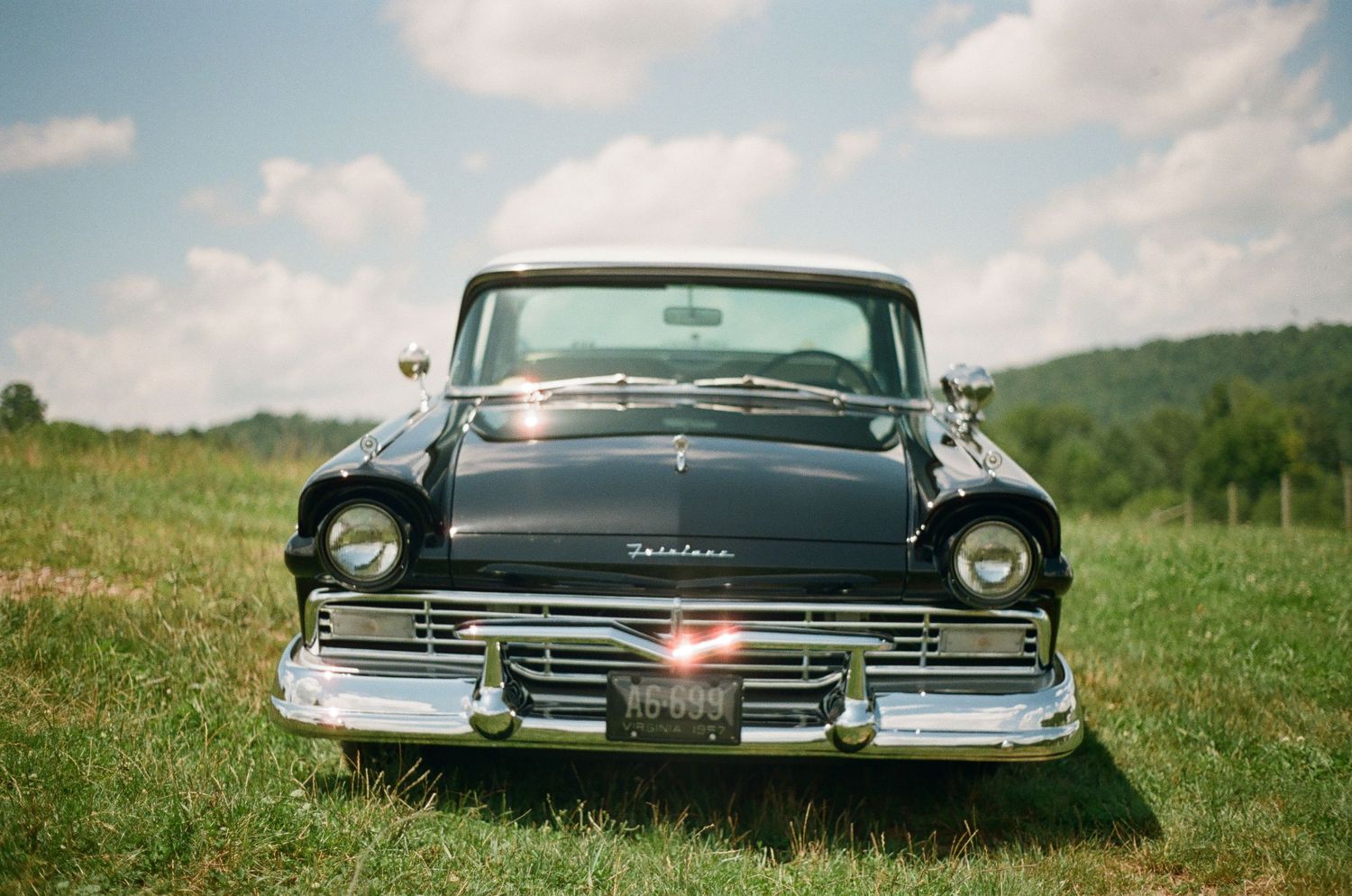 Front view of a pristine black 1950s Ford with chrome trim parked in a grassy field.
