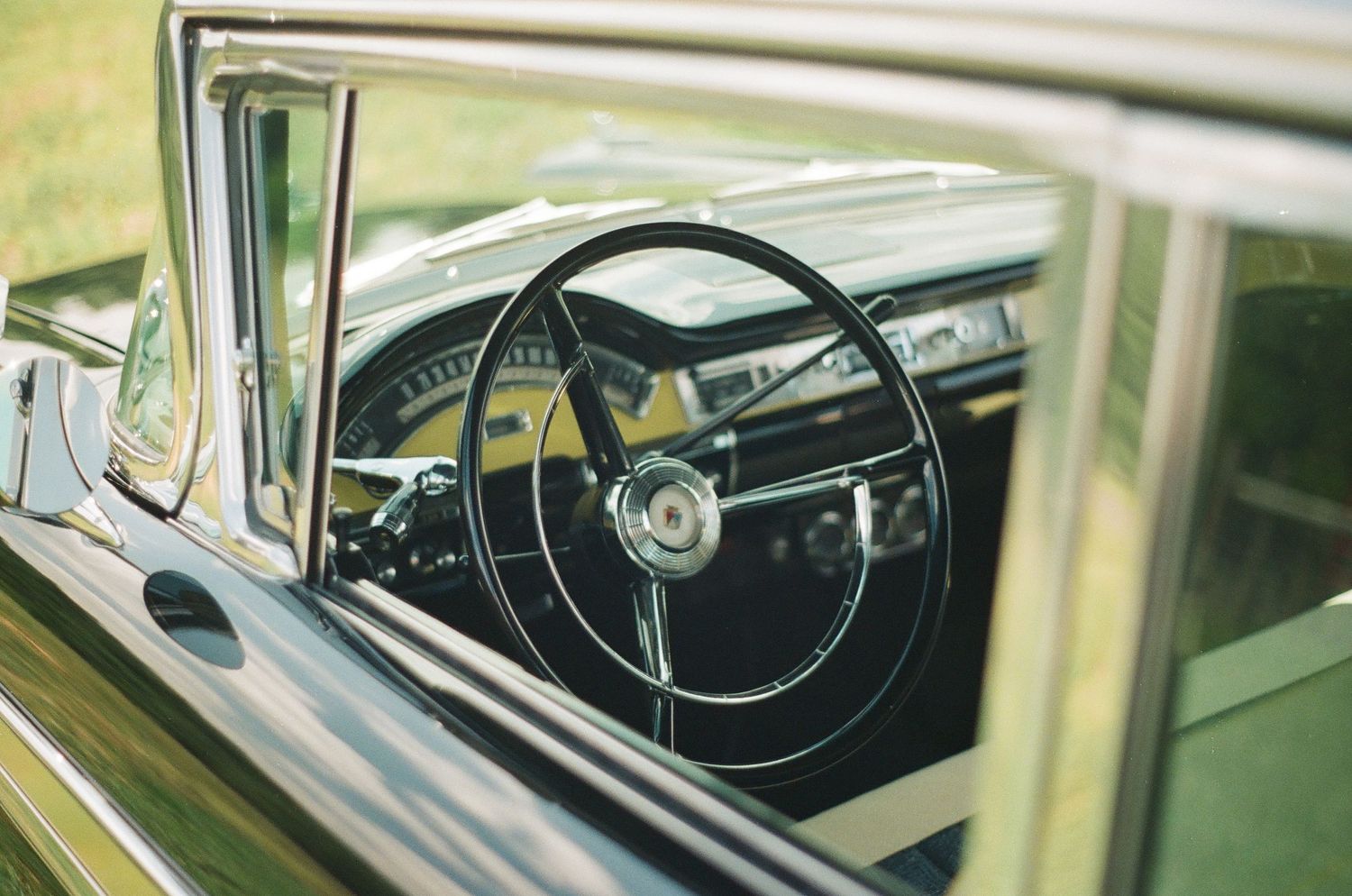 Interior shot through car window showing vintage steering wheel and dashboard details.