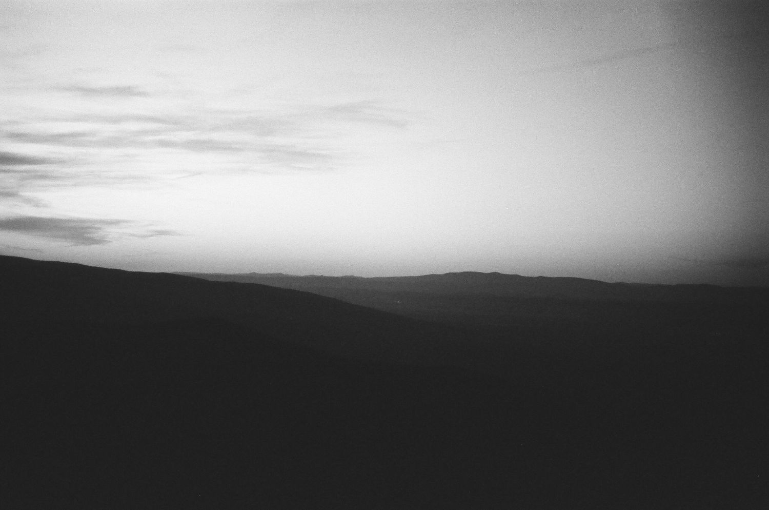 Black and white landscape photograph of rolling hills silhouetted against a dusky sky.