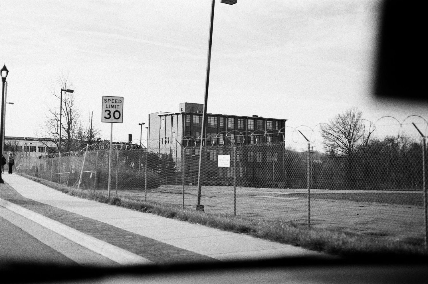 Black and white urban scene showing an abandoned building behind a chain-link fence.