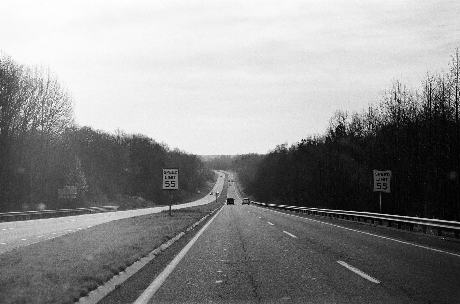 Empty highway stretching into the distance between wooded areas in black and white.