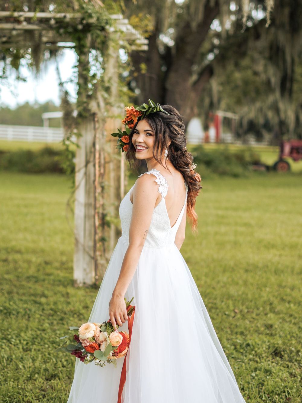 Elegant bridal portrait with vibrant floral crown and flowing white gown in a garden setting.