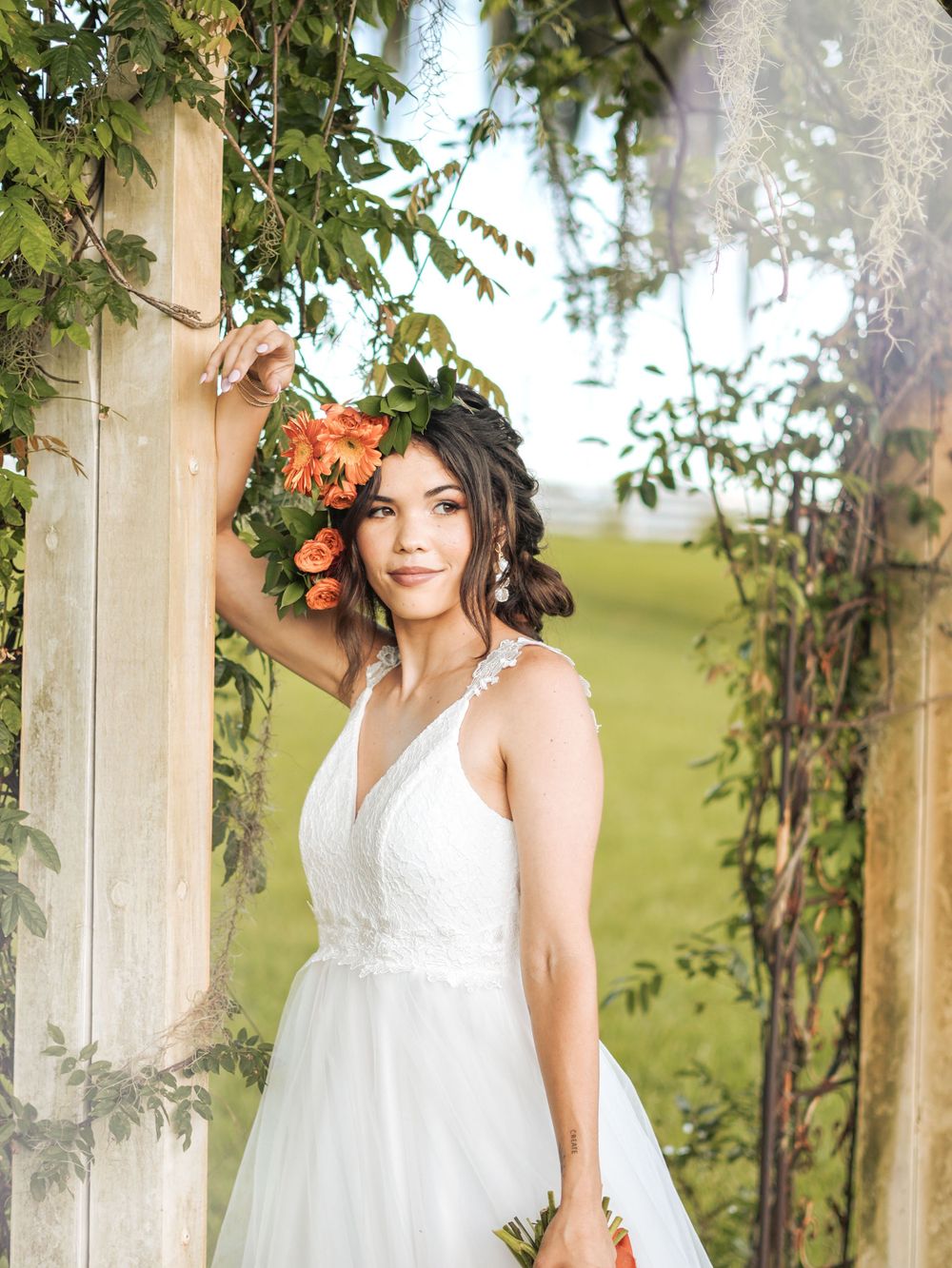 Close-up bridal portrait with coral flowers and white dress against a garden backdrop.