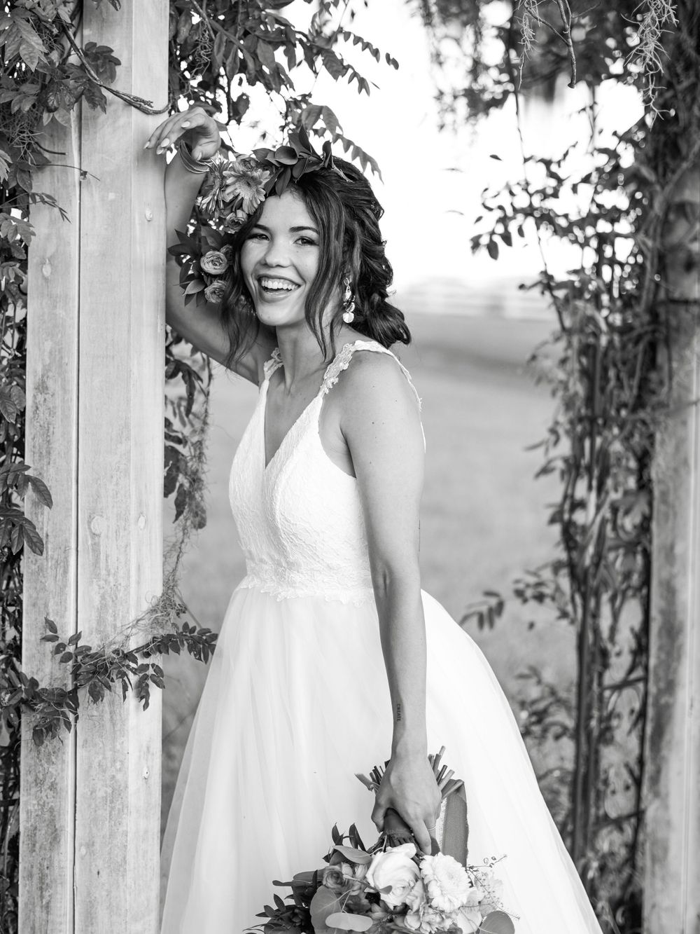 Black and white portrait of a joyful bride posing among climbing vines.