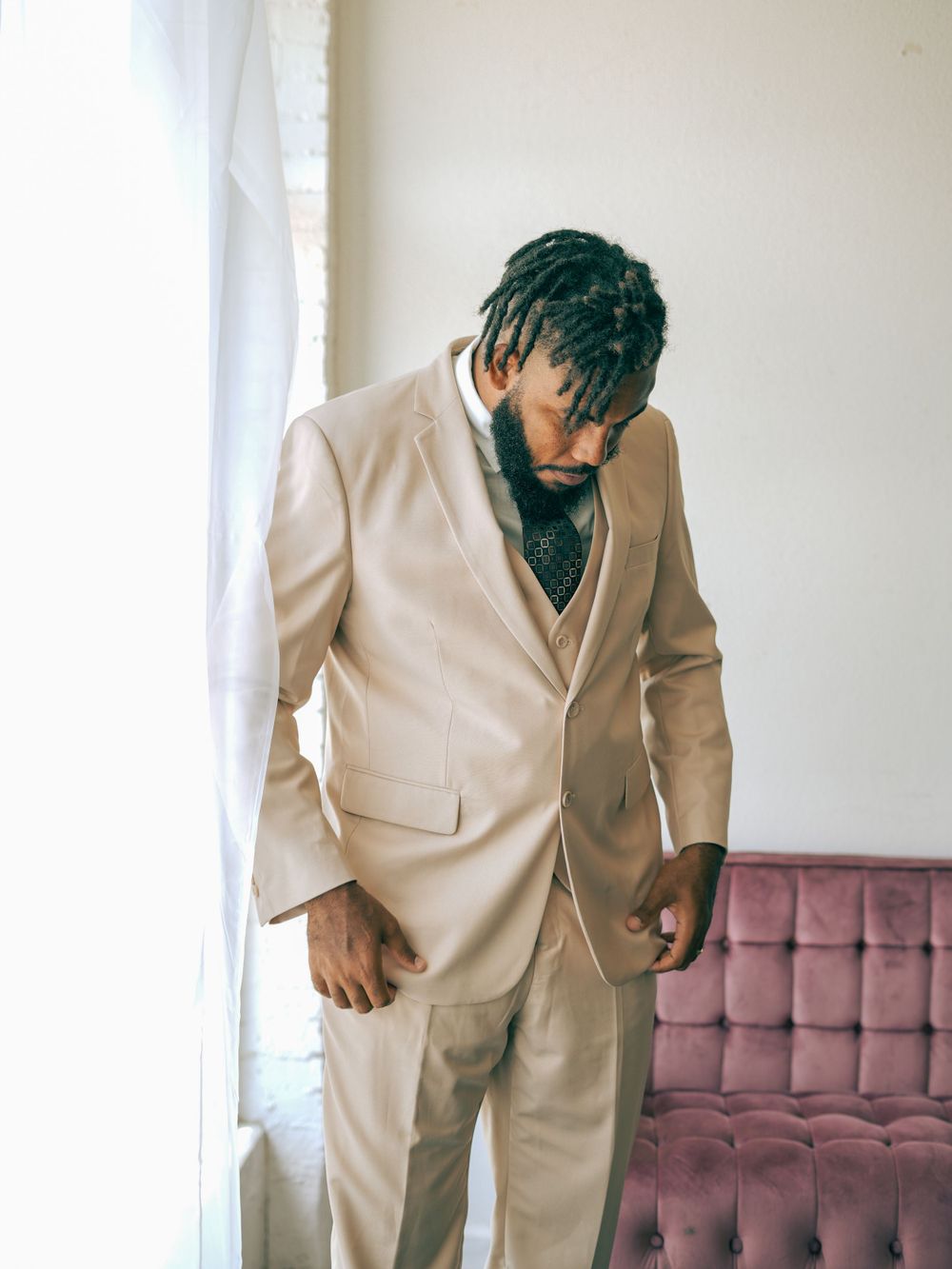 Man in beige suit looking down pensively in minimalist indoor setting.