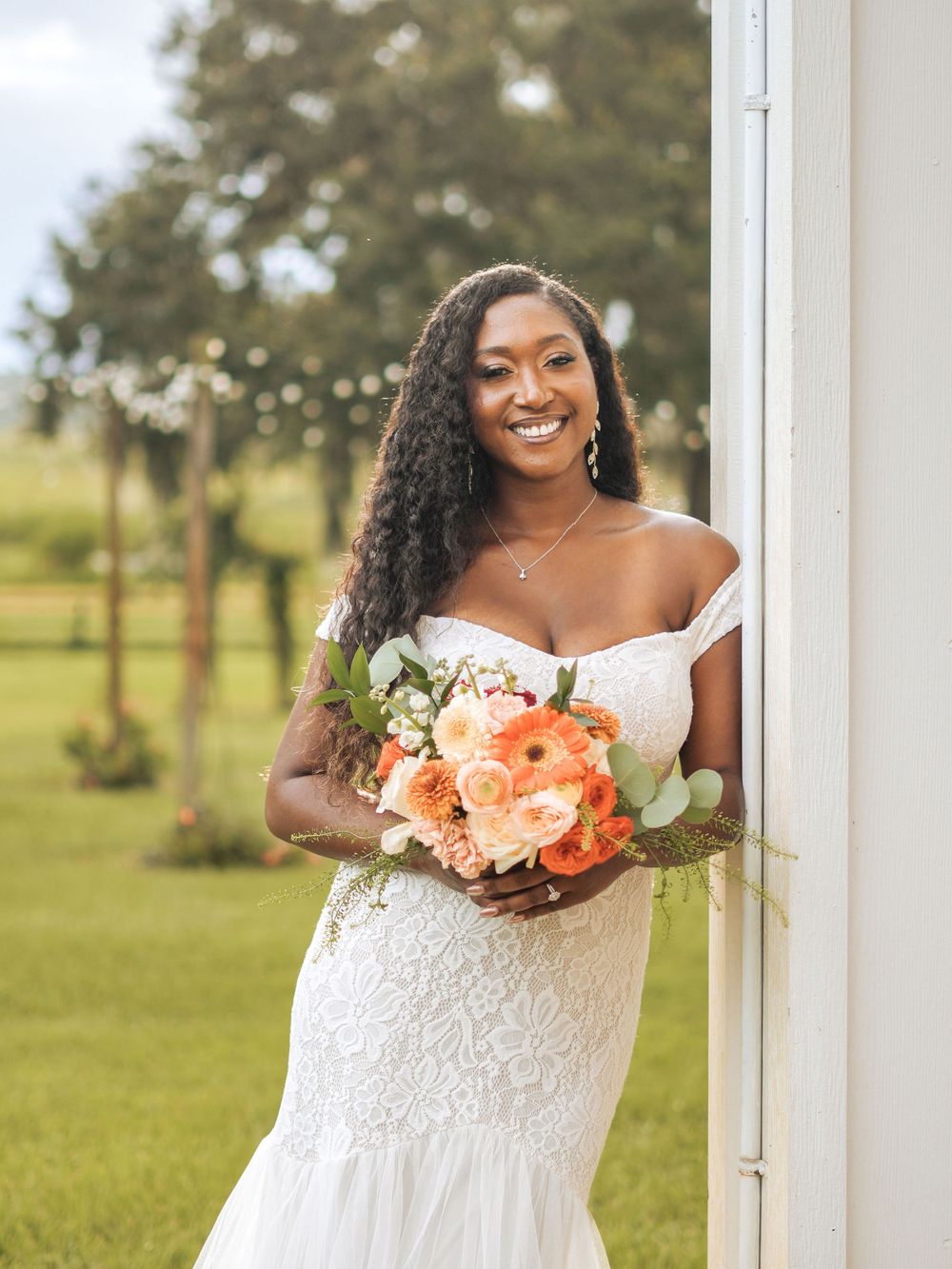 Radiant outdoor bridal portrait with coral bouquet and off-shoulder lace gown.