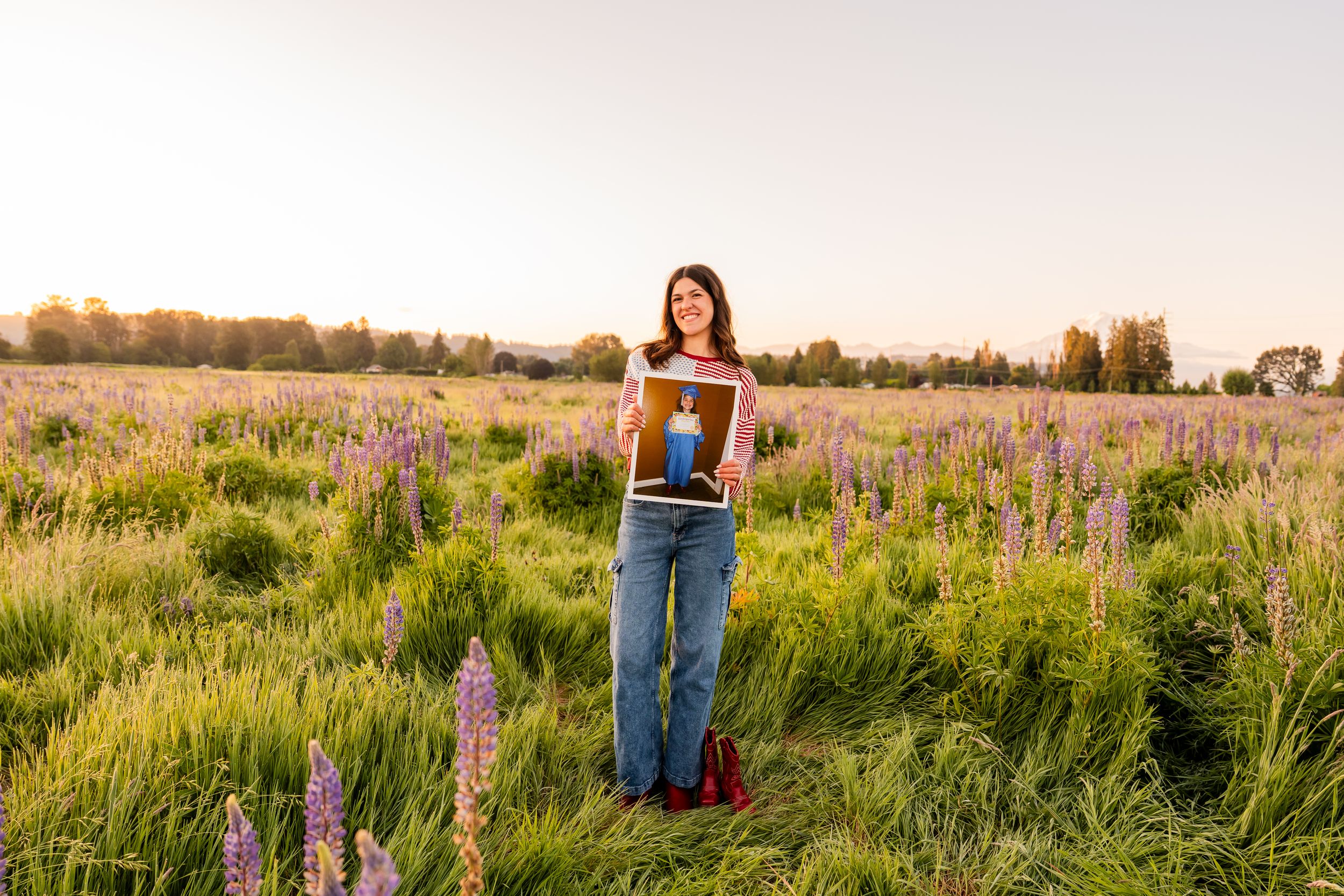 Woman holding framed photo in purple lupine field at golden hour sunset.