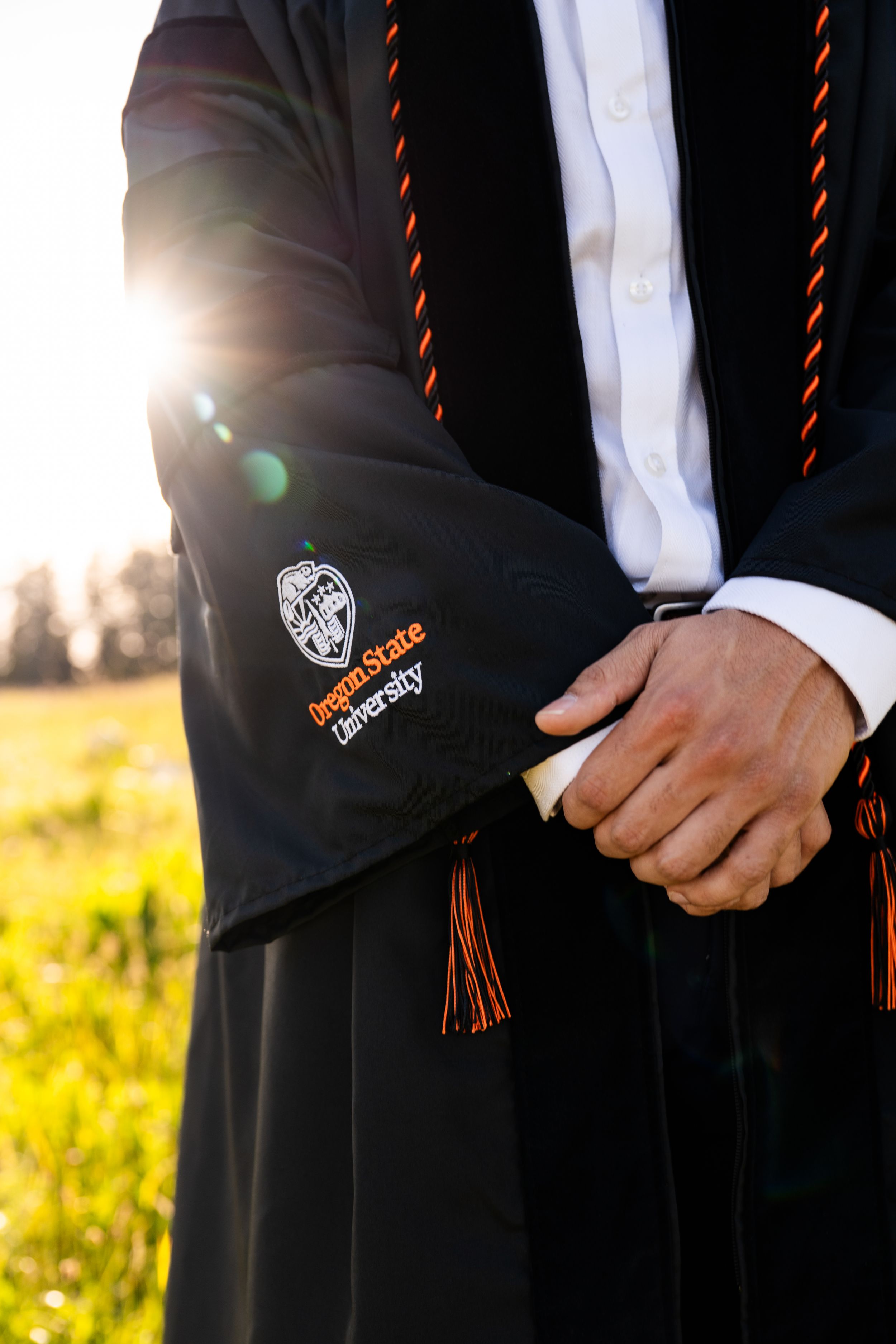 Oregon State University graduate in black gown holding diploma outdoors with sunlight in background.