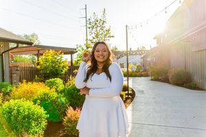 A person in a white dress walks through a sun-drenched garden path with blooming yellow flowers and greenery.