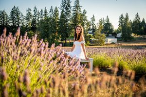 A white sundress stands out against vibrant purple lavender fields with evergreen trees in the background at sunset.