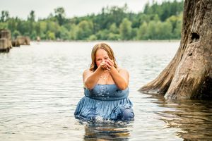 A woman in a blue dress poses in a lake surrounded by cypress trees during a dreamy outdoor photoshoot.