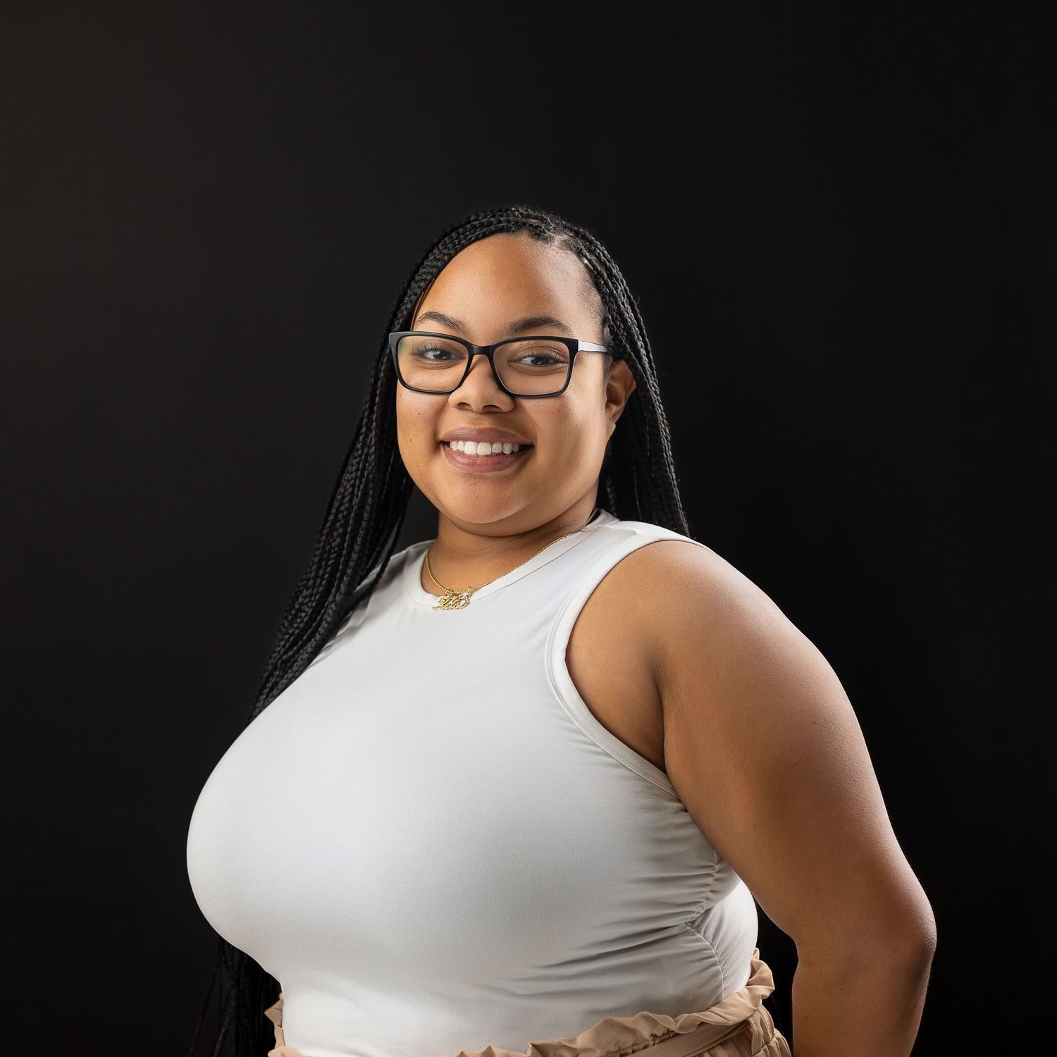 Professional studio portrait against black background showing person in white sleeveless top smiling warmly with glasses.