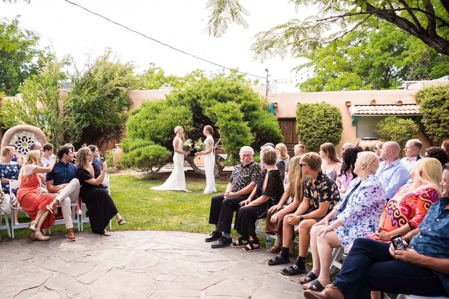 Lesbian couple walking down the aisle at their intimate wedding ceremony in the lush garden courtyard of Casas de Suenos