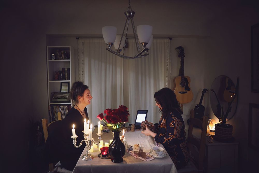 A candlelit table scene with two people looking at digital devices surrounded by candles and roses.
