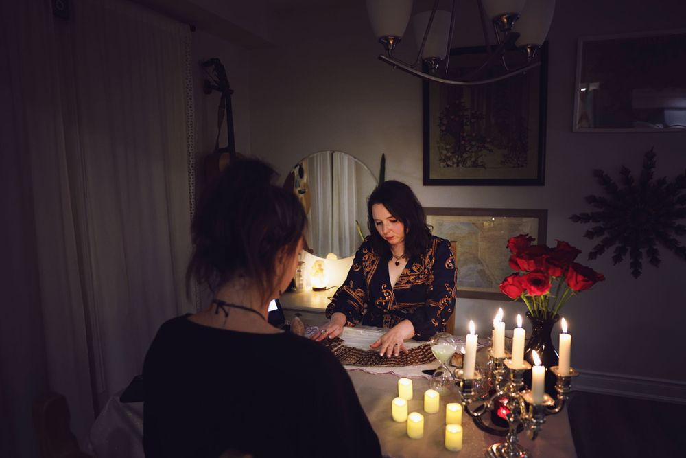 A dark atmospheric scene with candles and tarot cards being read at a table.