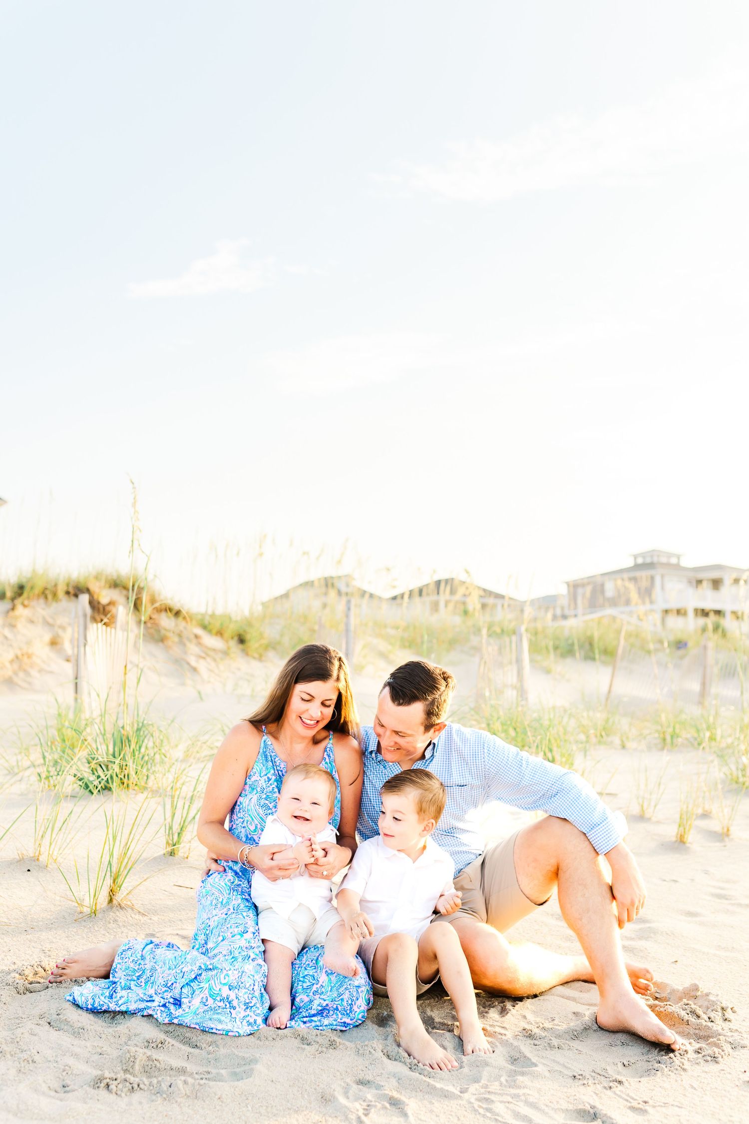 Family relaxing together on sandy desert terrain during sunset photoshoot in casual summer attire.