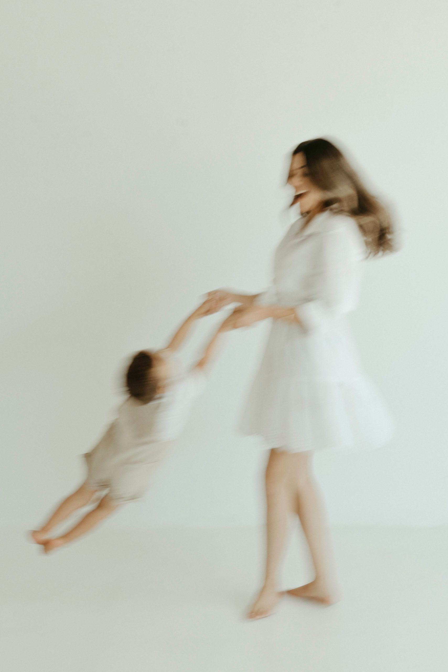 A series of blurred motion photographs showing a figure in white dress spinning and moving against a light background.